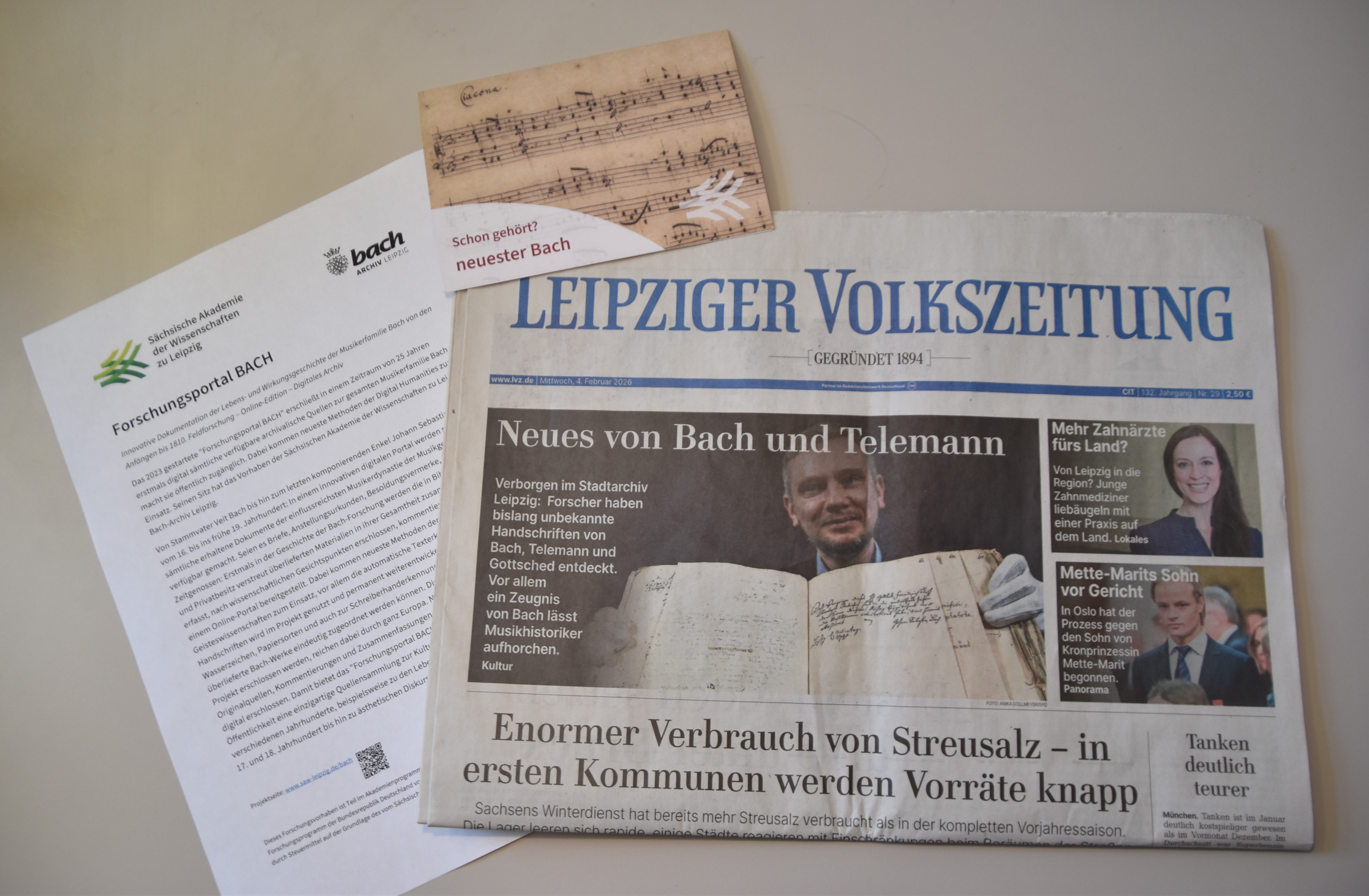 Auf einem Tisch liegen die Leipziger Volkszeitung mit dem Aufmacher-Artikel "Neues von Bach und Telemann", eine Klappkarte der Akademie ("schon gehört? neuester Bachund ein A4-Blatt mit Informationen zum Forschungsportal BACH.