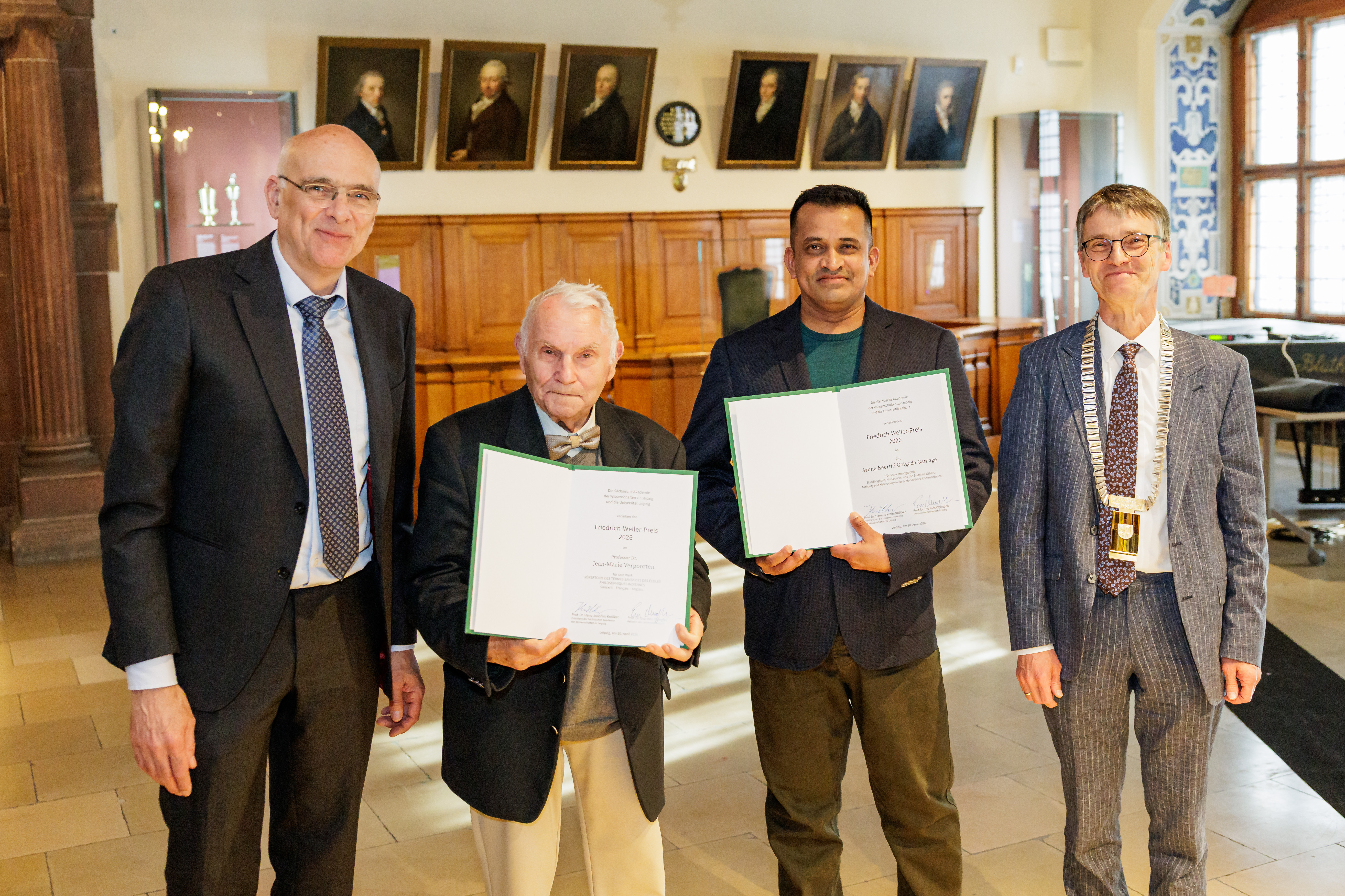 Vier männliche Personen stehen lächelnd in einem Festsaal, zwei von ihnen halten Urkunden in den Händen. Die männliche Person rechts trägt eine goldene Amtskette.