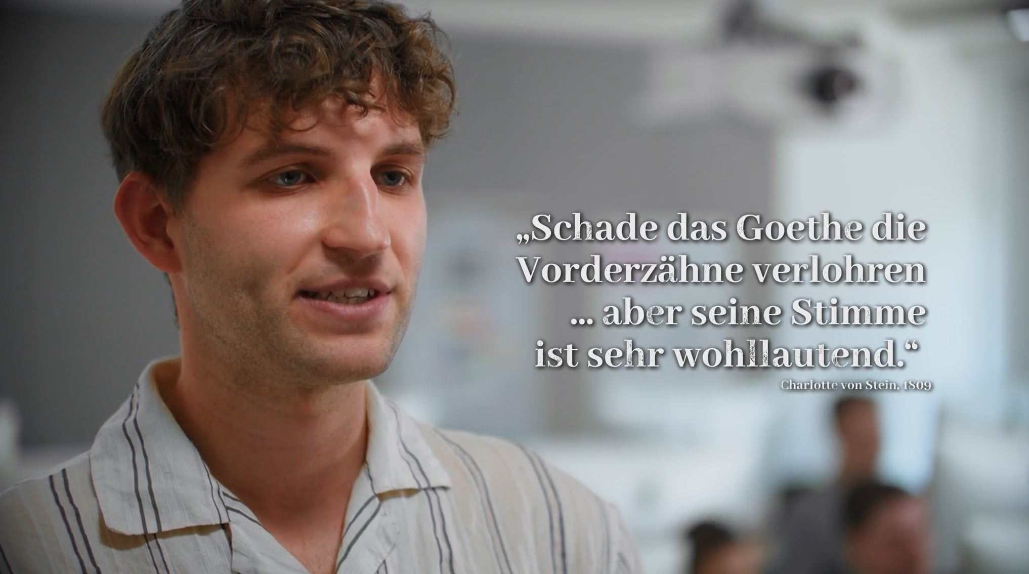Eine männliche Person spricht in die Kamera. Rechts daneben ist folgendes Zitat zu lesen: "Schade das Goethe die Vorderzähne verlohren ... aber seine Stimme ist sehr wohllautend." Charlotte von Stein. 1809