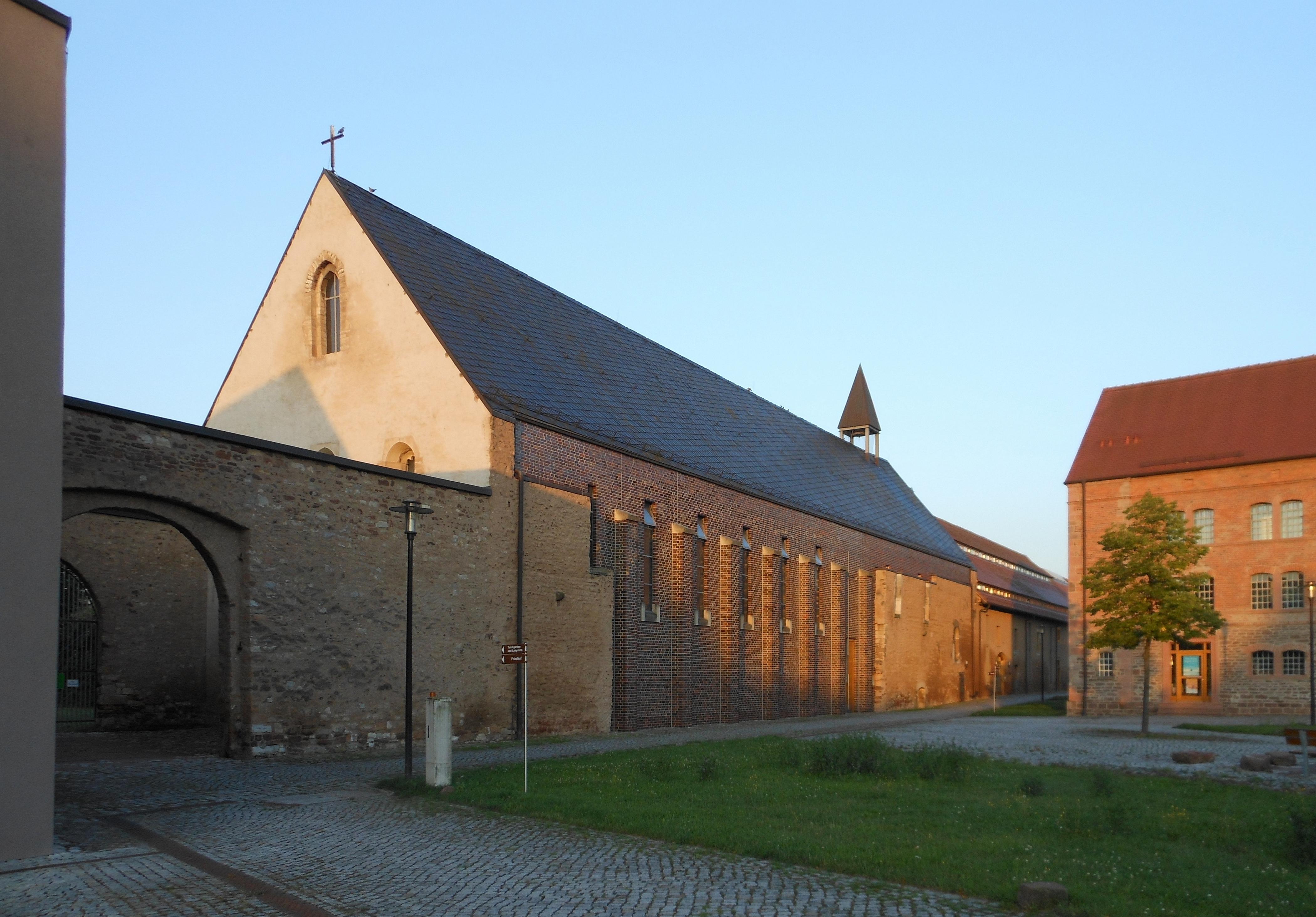 Die Kirche in Helfta mit einer Rasenfläche davor und einem Tor neben der Kirche auf der linken Seite des Bildes
