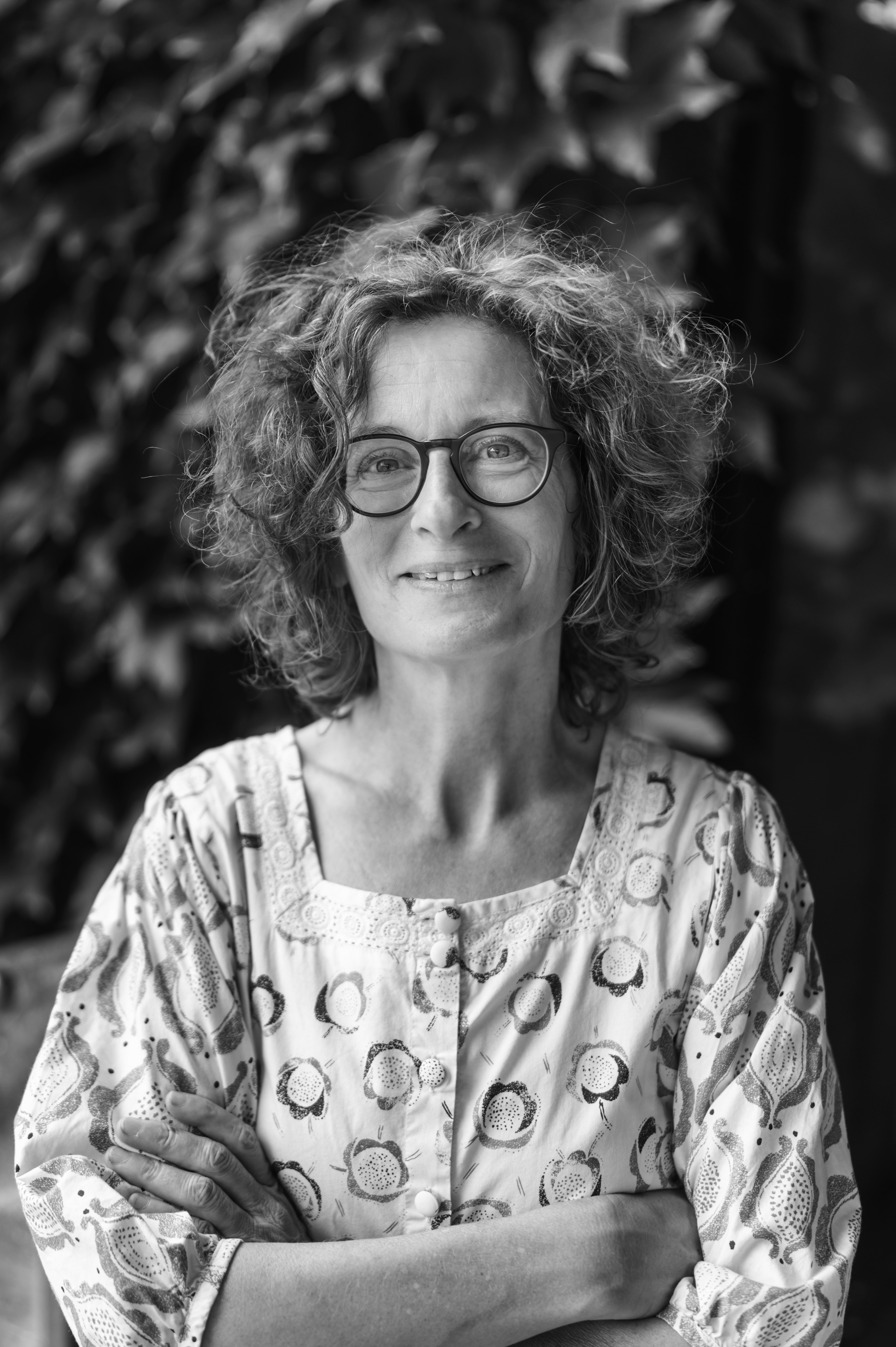 Schwarz-weiß-Porträtfoto von einer Frau mit Brille vor Pflanzen