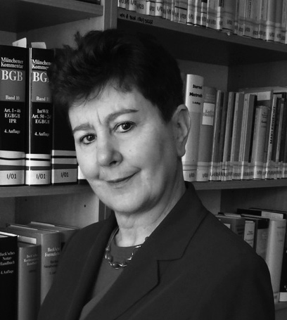 A black-and-white portrait photograph of a woman in front of a bookshelf
